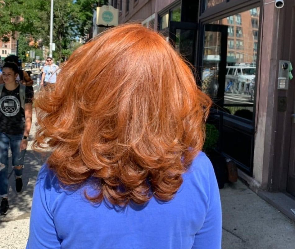 back view of a woman in a bright blue top with medium length pumpkin spice colored hair