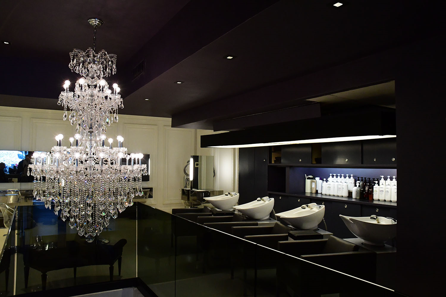 black hair salon with white sinks and a large chandelier