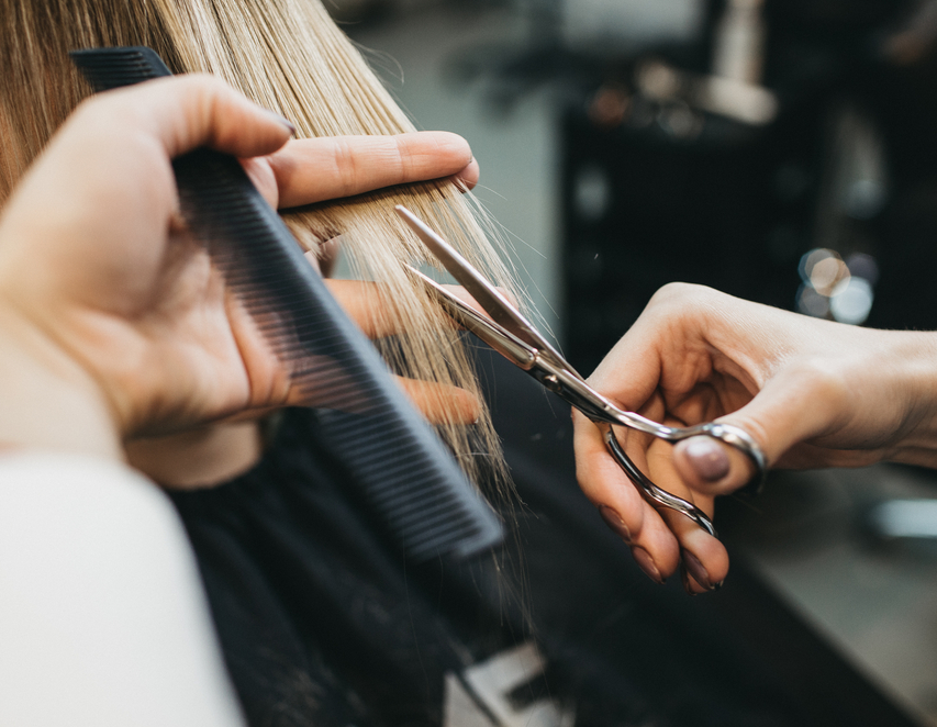hair stylist holding scissors and a comb cutting blonde hair
